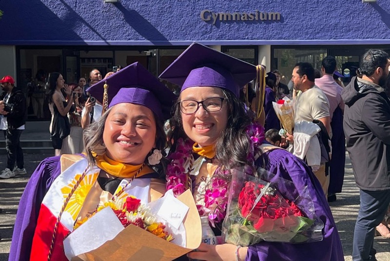 SEO scholars Judy Abuel and Marisol Flores smiling and posing for photo together in front of gymnasium