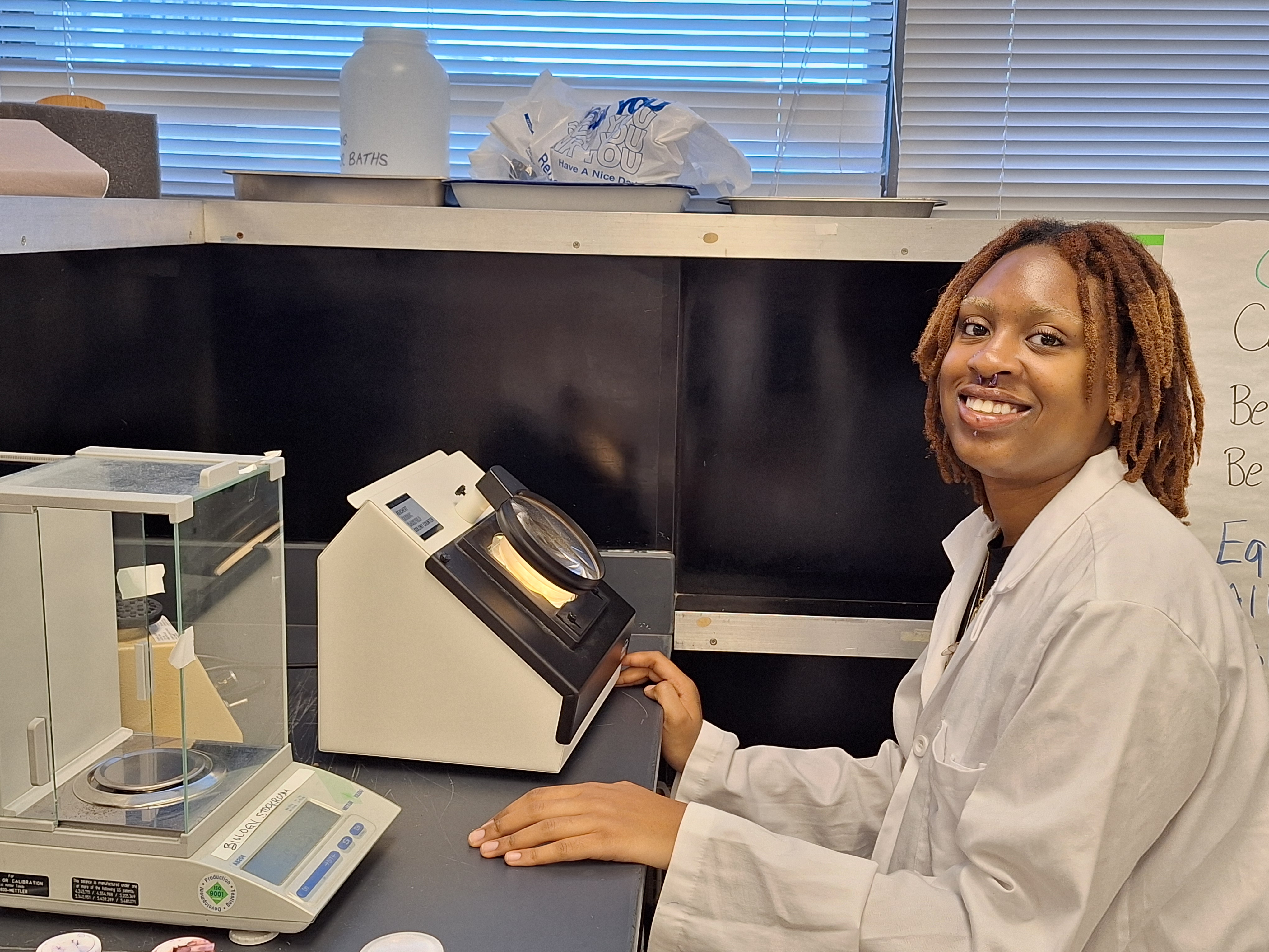 Student sits at plate magnifier in lab coat.